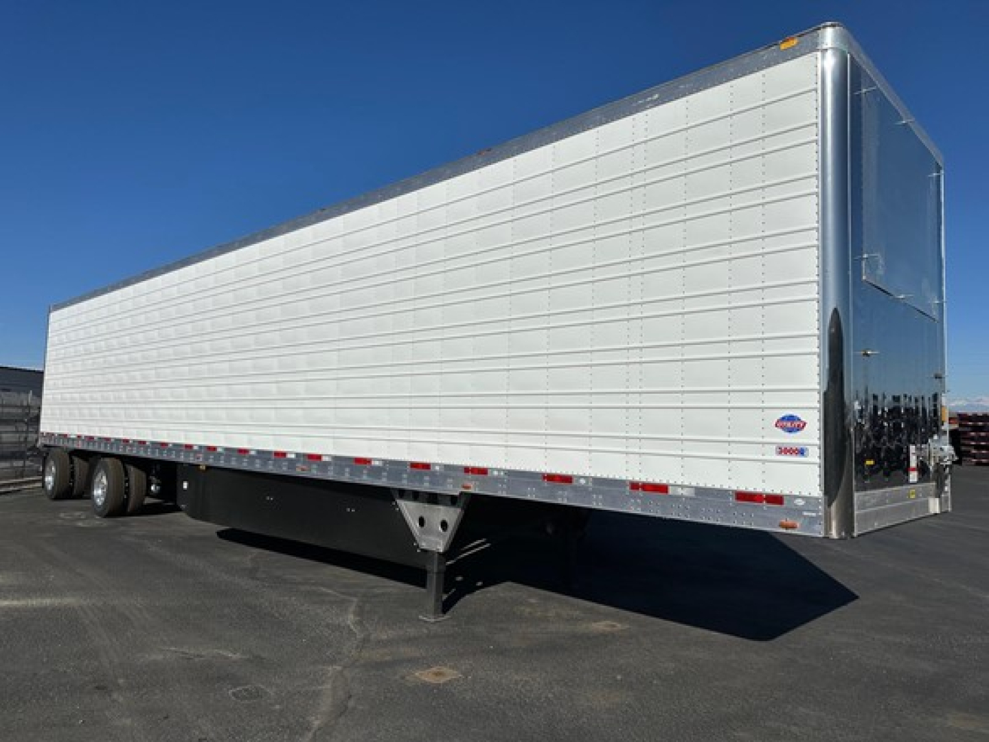 Utility 3000R trailer side view showing white panel walls with reflective tape, rear doors, and black landing gear at front; vendor logo visible near rear.