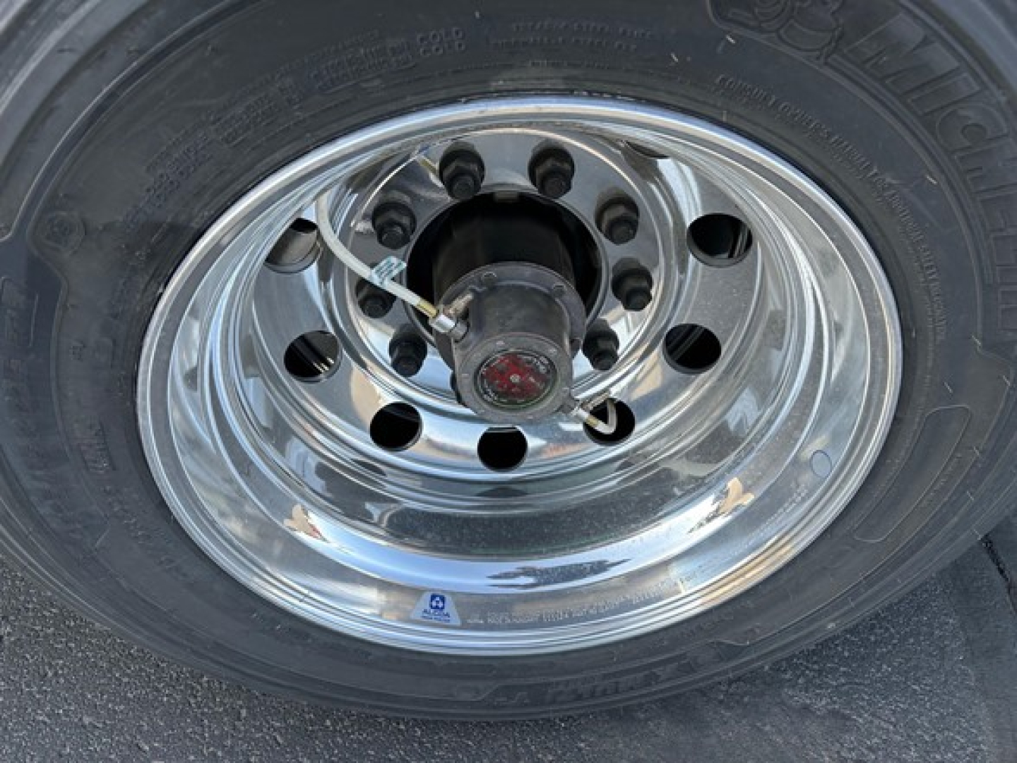 Wheel hub and tire of a utility trailer showing polished chrome rim and black tire with valve stem and lug nuts