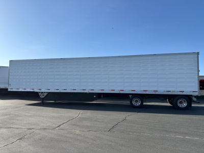 Long white refrigerated trailer with raised side panels and dual rear axles parked on pavement.