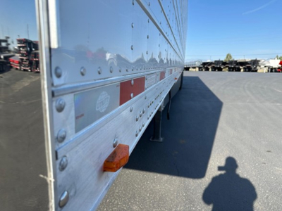 Trailer side of a new 2026 Utility 3000R reefer trailer showing riveted aluminum siding, orange reflectors, and support legs in a storage lot.