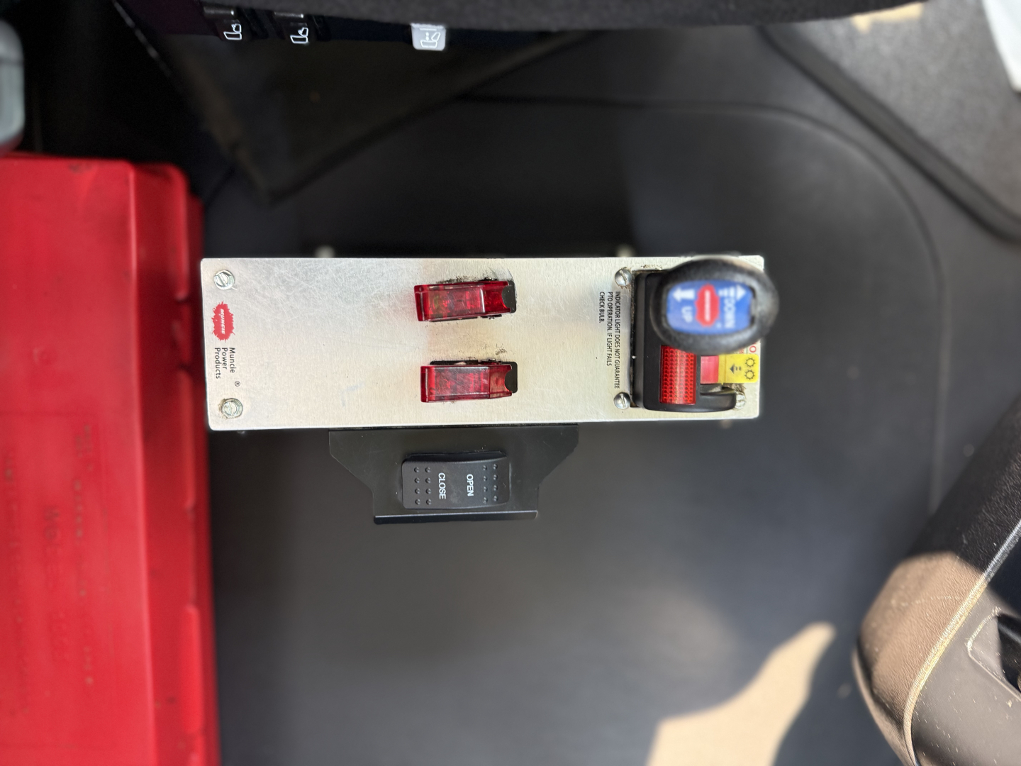 Panel showing control switches and a blue and red dial on a Mack AN64T truck cab interior with metal toggle switches and a black switch.