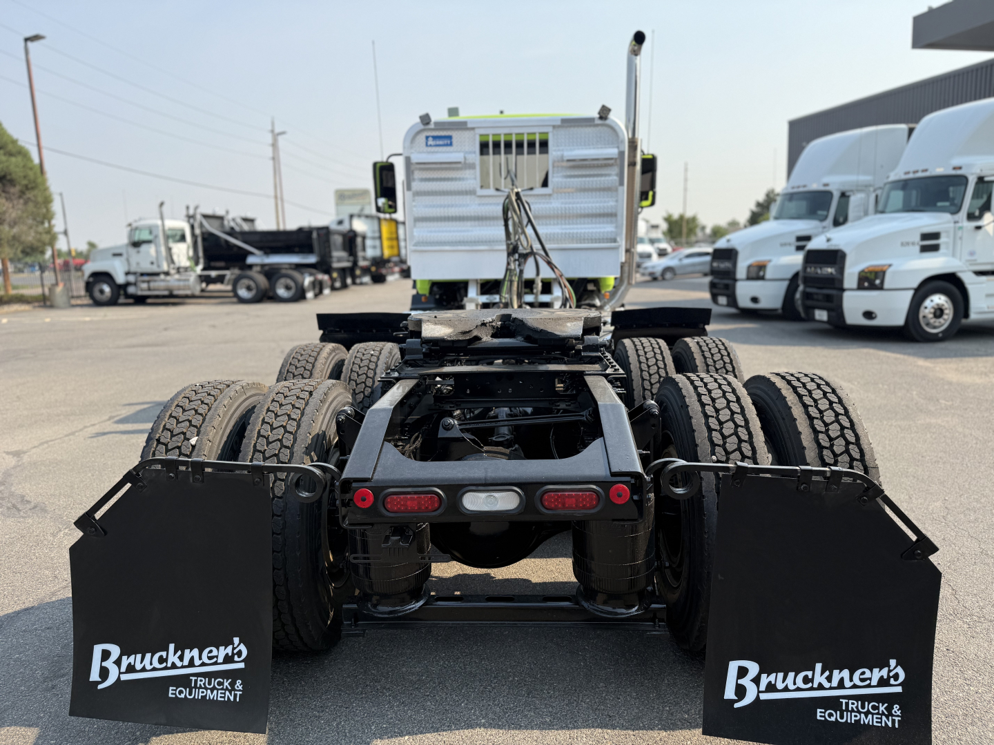 Rear view of a used 2025 Mack AN64T daycab chassis showing dual rear axles, mud flaps with Bruckner's logo, and fifth-wheel area in a truck yard.