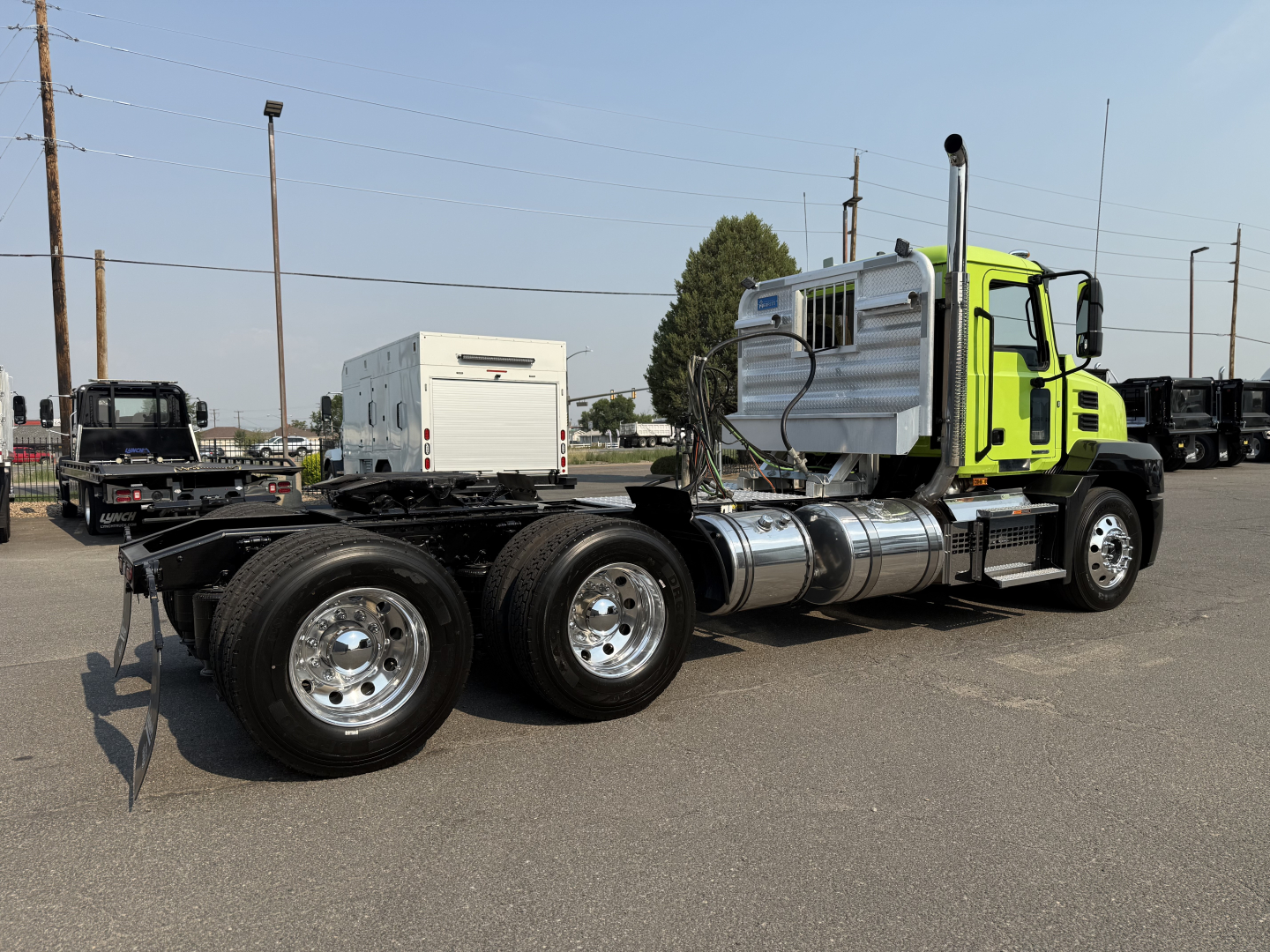 Truck tractor side view showing bright green cab, dual rear axles, chrome tanks, and exhaust stack on a flat lot.