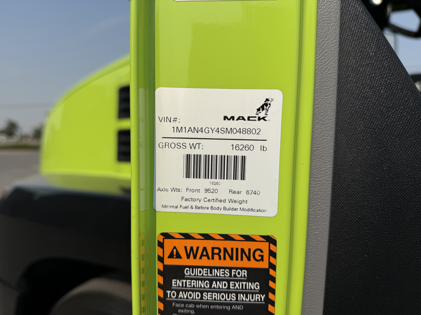 VIN label on a green Mack AN64T showing VIN 1M1AN4GY4SM048802 and gross weight 16260 lb with a warning sticker below about entering and exiting to avoid serious injury.
