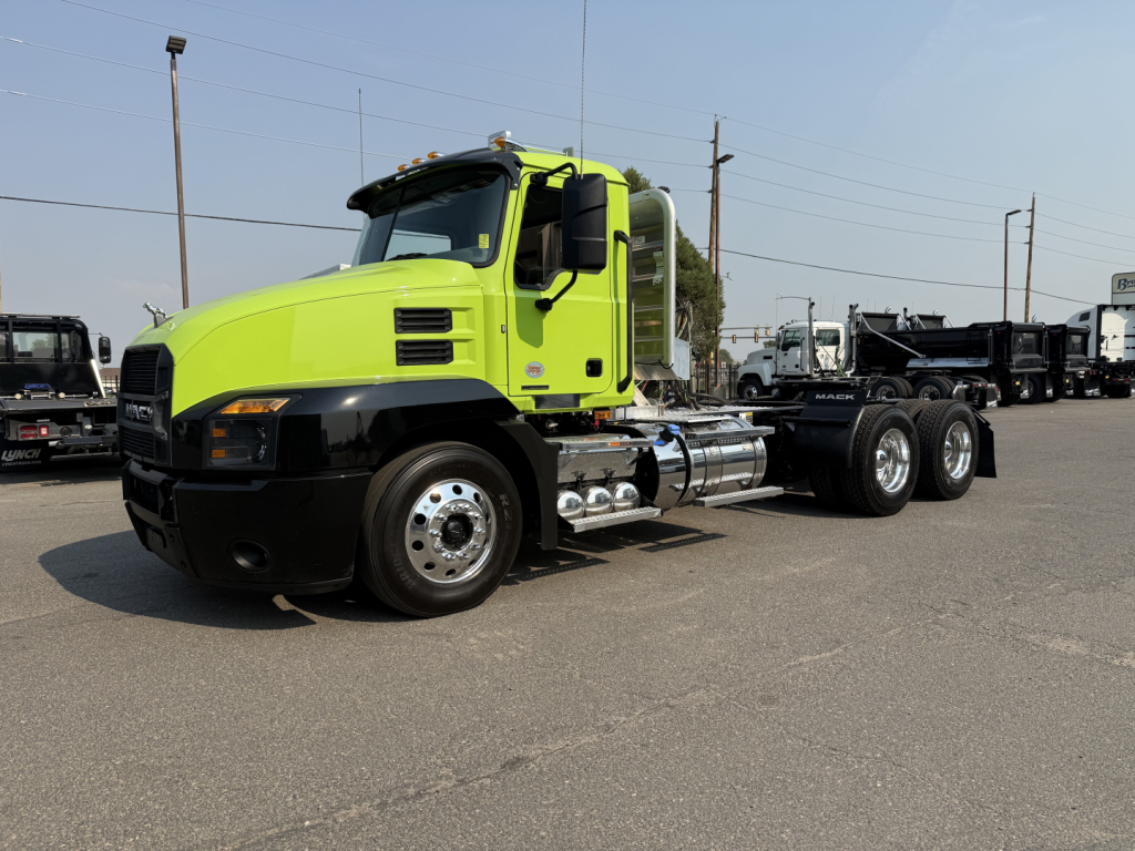 Mack AN64T conventional day cab truck with lime green cab and chrome fuel tanks, three rear axles, side exhaust visible.