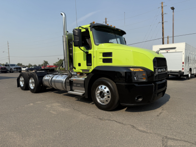 Green Mack AN64T conventional daycab tractor with chrome exhaust stack and fuel tanks visible, front-right view showing Mack grille and bumper.
