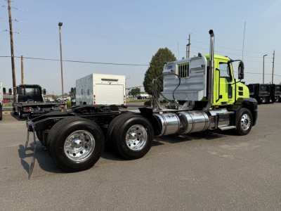 Truck tractor side view showing bright green cab, dual rear axles, chrome tanks, and exhaust stack on a flat lot.