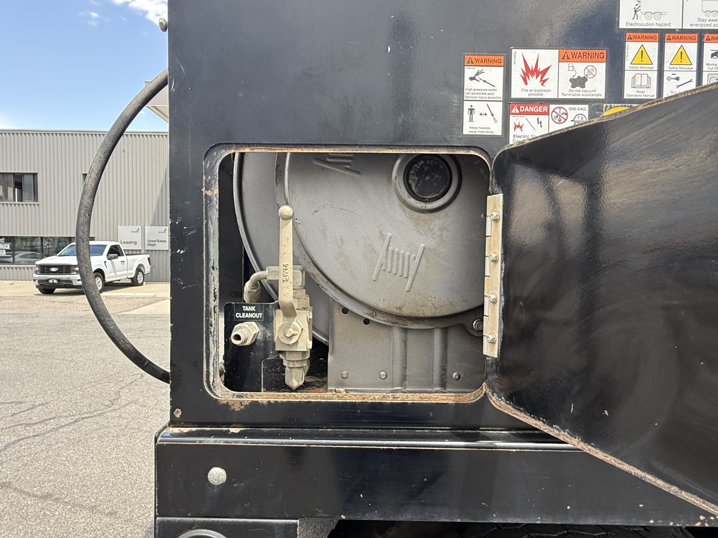 Mack GR64B vacuum truck rear-side compartment with circular tank hatch and warning labels.