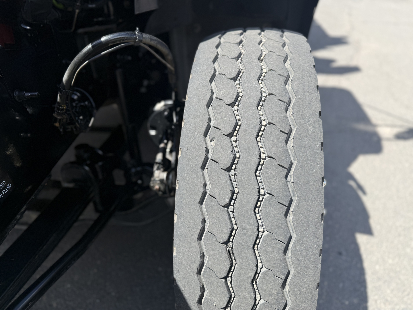 Front tire of a Mack GR64B truck showing tread pattern and suspension components.