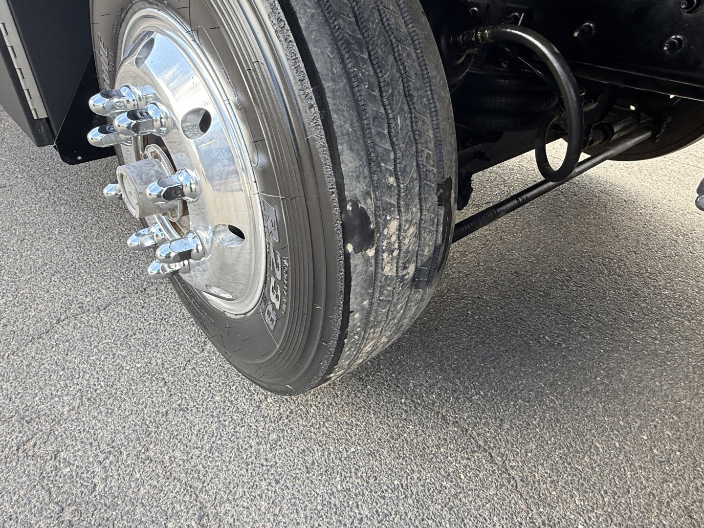 Front wheel and suspension of a Mack GR64B truck showing tire tread and chrome lug nuts.