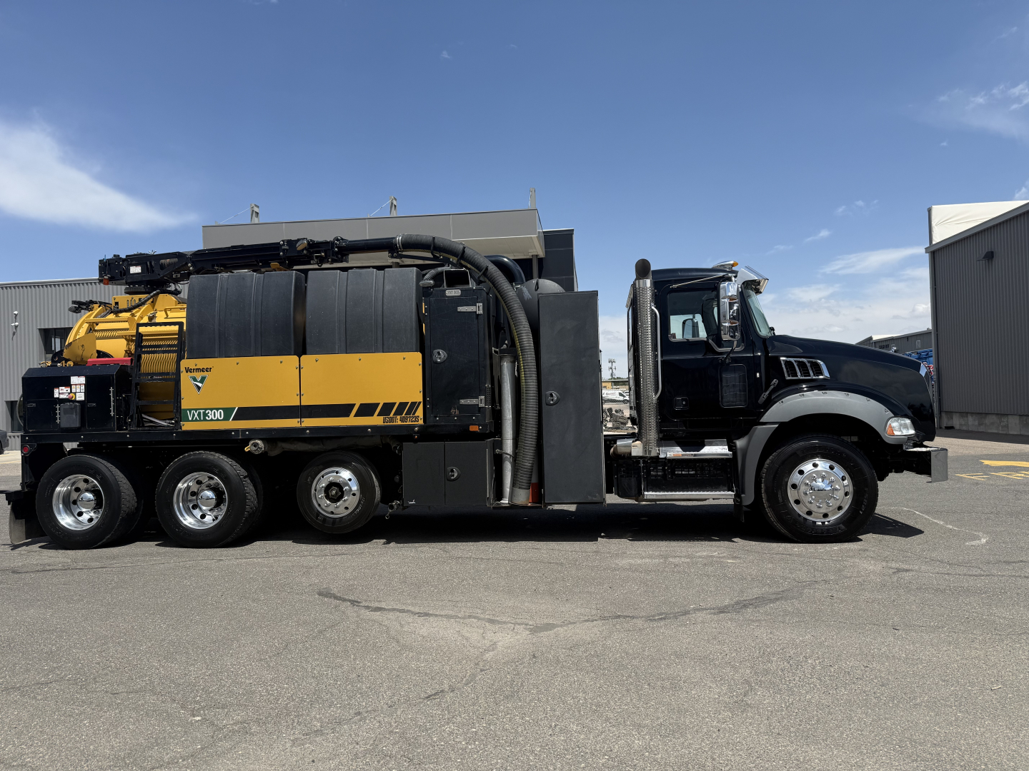 Side view of a 2023 Mack GR64B vacuum truck with yellow and black vac system components mounted on a black truck chassis. Visible labels include 'VER'.