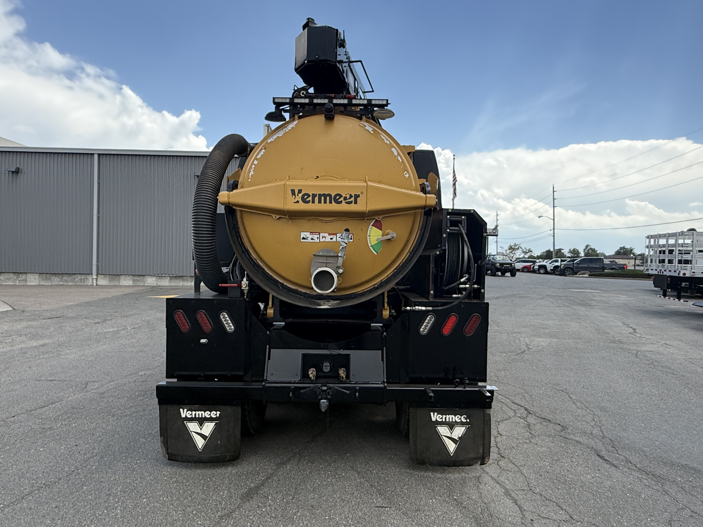Rear view of a 2023 Mack GR64B vacuum truck trailer with a circular beige tank labeled Vermeer, mounted on a black chassis with mud flaps and hoses visible.