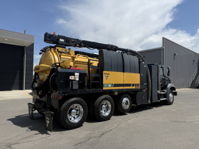 Mack vacuum truck chassis showing large yellow vacuum compressor unit with black hoses and reel, multiple axles, side view.