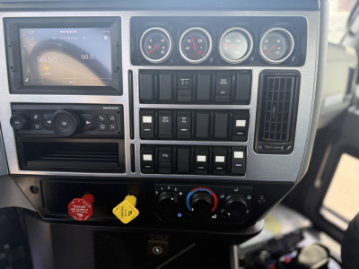 Dashboard of a Mack GR64B truck showing gauges, radio display, numerous control switches, climate controls, and ignition/auxiliary switches.
