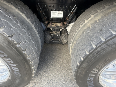 Rear view undercarriage showing dual rear wheels and drivetrain components of a Mack GR64B truck, with label placard mounted on frame between axles.