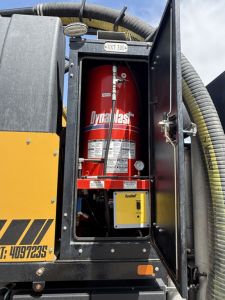 Rear cabinet showing a red Dynastat fire extinguisher mounted inside a black compartment with yellow exterior paneling and hoses.