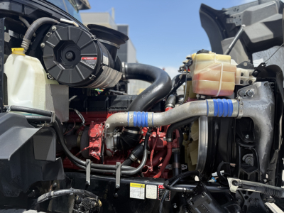Mack GR64B truck engine bay showing cooling reservoir, hoses, and diesel engine components; labels on hoses and a red engine block visible.