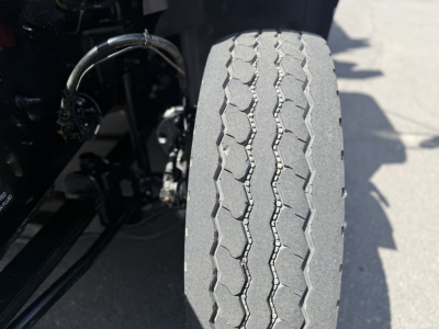 Front tire of a Mack GR64B truck showing tread pattern and suspension components.