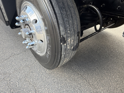 Front wheel and suspension of a Mack GR64B truck showing tire tread and chrome lug nuts.