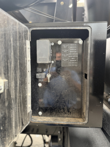 Electrical panel/label inside a small access box on a Mack GR64B truck. Visible text on a metal plate with rows of labels and a key switch nearby.
