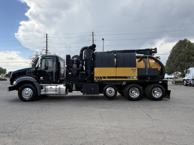 Mack GR64B vacuum truck side view showing large yellow and black tank with hoses and chrome exhaust, cab front chrome bumper, and multiple axles.