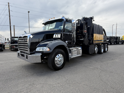 Mack GR64B vacuum truck side view showing large front grille, dual rear axles, black cab, and vacuum tank with hoses.