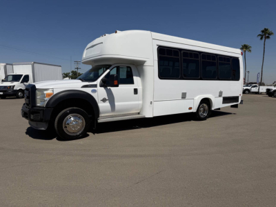 White Ford F-450 shuttle bus front left side with raised roof, black window tint, and wheel well; side windows and passenger door visible.