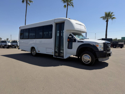 Ford F-450 shuttle bus side view showing front doors open, white body, black wheel arches, chrome wheels, and windows along passenger area.
