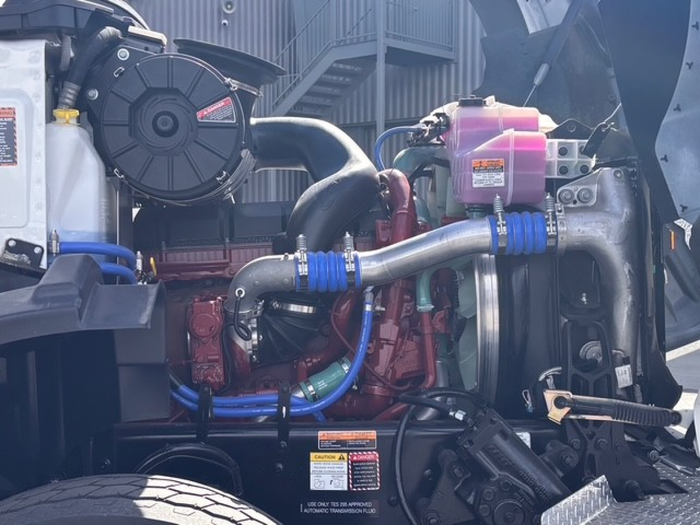 Mack GR64B engine bay showing coolant reservoir, intake tubes, hoses, and turbo/engine components.