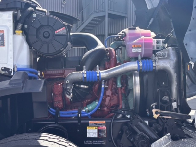 Mack GR64B engine bay showing coolant reservoir, intake tubes, hoses, and turbo/engine components.