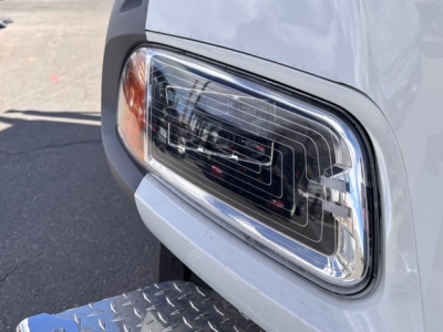 Front headlight assembly of a 2026 Mack GR64B roll-off truck showing clear lens with chrome housing and surrounding body panel.