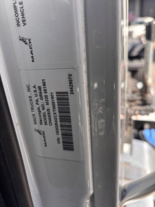 Mack GR64B label visible on door frame with VIN and stock number; label shows 'MACK TRUCKS INC', 'MODEL GR64B', 'MACK TRUCKS', and barcode; text includes VIN 1M2GR4GCXTM051901 and stock 69128.
