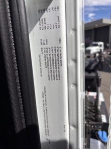 Label on Mack GR64B rollover truck showing GVW and axle weight ratings and serial/identification details on a metal plate inside the cab area.