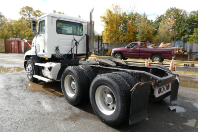 Truck chassis and cab of a 2004 Mack CX Vision CX613 with dual rear axles, concrete surface, and trees in background.