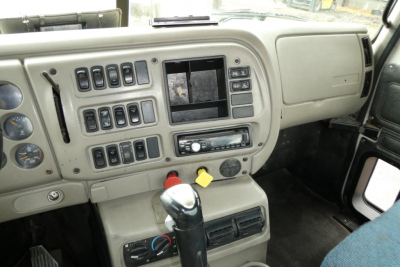 Cabin dashboard of a Mack CX truck showing multiple switches, center display, gear lever, control panels, and steering area.