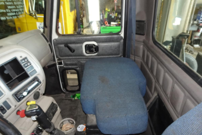 Vehicle cab interior showing bench seat folded forward in a Mack CX (Vision) CX613 truck. Dashboard, gear shifter, window, and door panel visible.