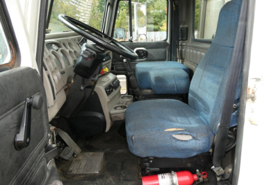 Cab interior of a 2004 Mack CX Vision CX613 daycab showing blue fabric seats, steering wheel, dashboard, and worn driver seat; basic controls visible.