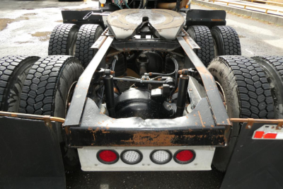 Rear view of a Mack CX Vision truck chassis showing dual rear axles, fifth wheel, and mud flaps with JNI fuel lines; warning lights and bumper visible.