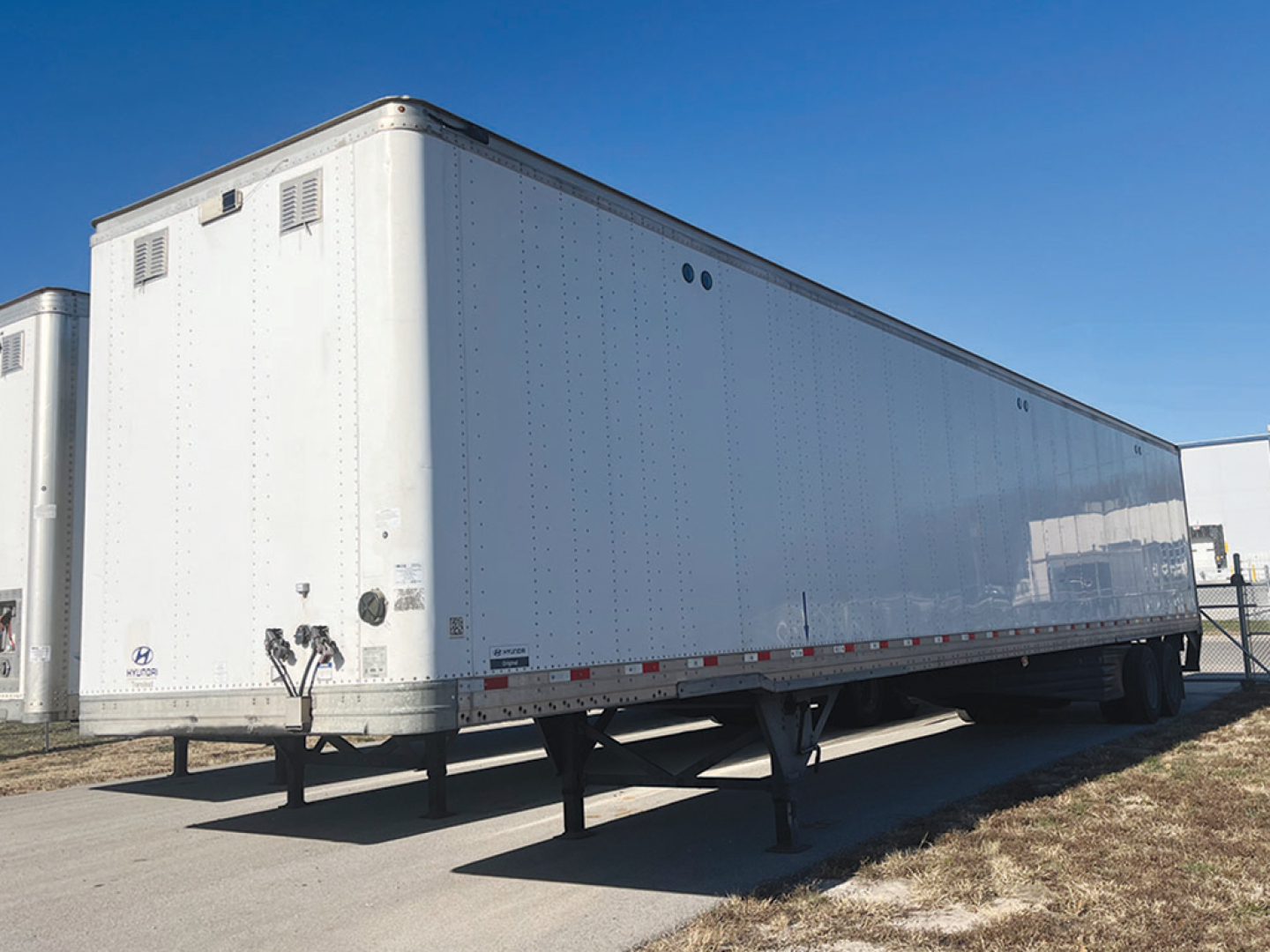 Trailer undercarriage and side view showing white enclosed trailer with support legs and DOT reflective tape.