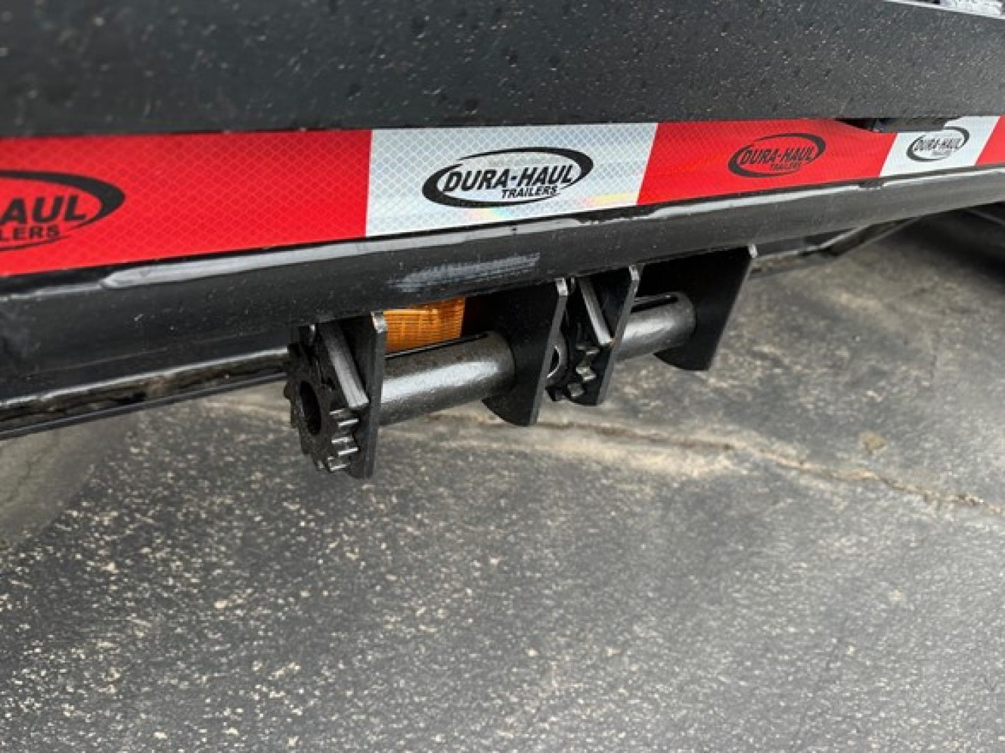 Drop deck trailer undercarriage showing Dura-Haul logo decals and bumper hitch area with reflective tape.