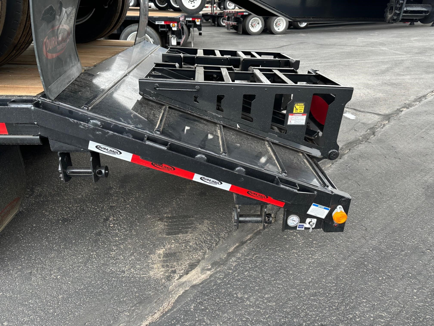 Trailer rear view showing drop deck with beaver tail and flip ramps, black steel construction, side accessories, and safety lights.