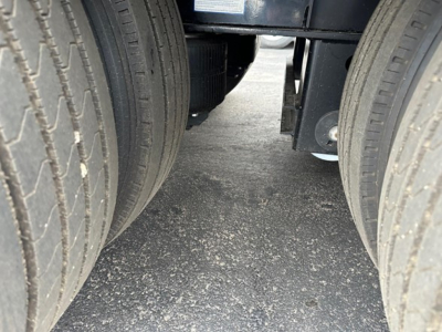 Front view undercarriage of a trailer showing dual rear tires and underbody frame with gravel road surface.