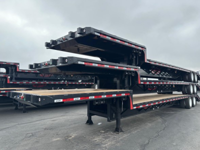 Drop deck trailer stacks showing multiple flatbed decks and steel frames, black with red/white reflective tape, under cloudy sky.