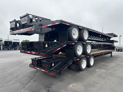 Trailer stack showing multi-axle drop deck trailer with three levels, black frame, white wheels, steel decking, mounted on a lot.