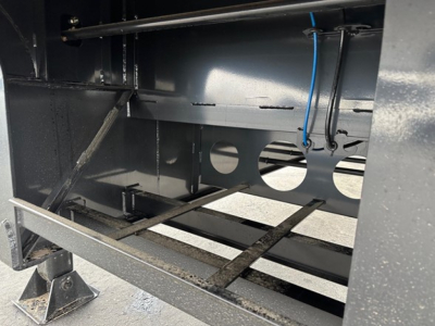 Drop deck trailer frame interior showing steel rails and underside with blue wiring harness and circular cutouts.