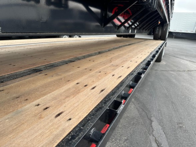 Drop deck trailer with wooden deck planks and steel edge rails showing cargo area perspective.