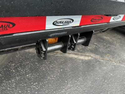 Drop deck trailer undercarriage showing Dura-Haul logo decals and bumper hitch area with reflective tape.