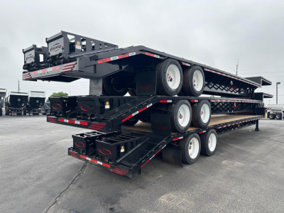Flatbed trailer stack showing multi-axle drop deck with beaver tail and flip ramps, black steel with reflective tape.