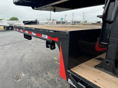 Flatbed trailer edge with wooden deck and black steel frame showing reflective red-and-white stripes and safety lights/receivers.