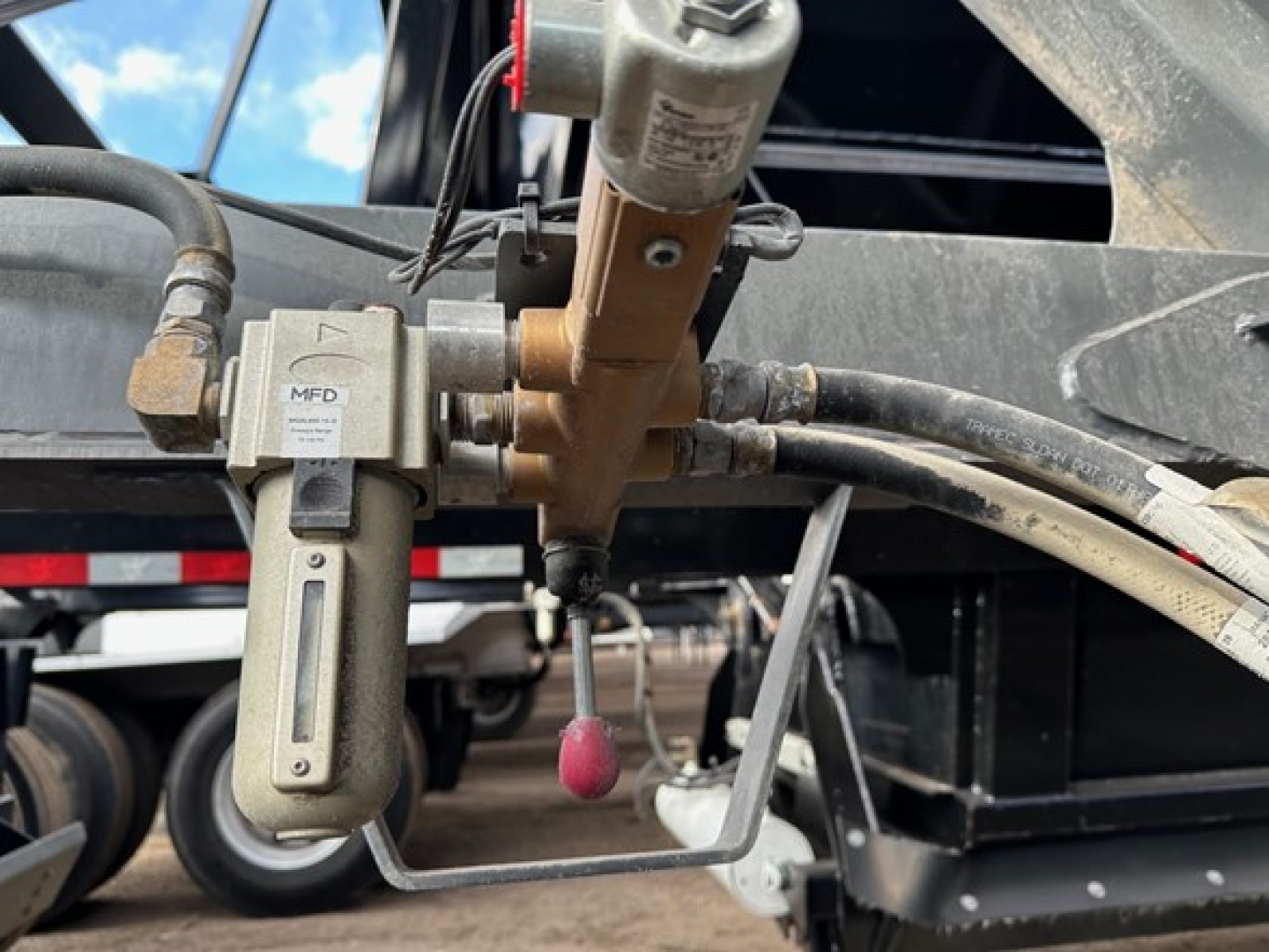 Bottom dump trailer hydraulic valve assembly with hydraulic hose and fittings, MFD label, and nearby metal frame components.